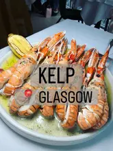 A high-quality, overhead shot of a plate of langoustines in a butter sauce, served with a charred lemon, at Kelp in Glasgow.