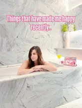 A lifestyle-focused image featuring a woman relaxing in a marble-tiled hotel bathroom, accompanied by a glass of juice and a tablet. The aesthetic is clean, bright, and aspirational, typical of travel or hotel-based influencer content.