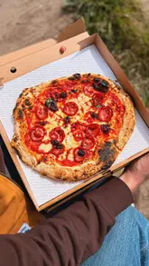 A couple visits a home-based pizza pop-up called Backyard Dough Co in Barry, Wales. The video documents the pizza-making process, the creator's setup, and the final product, which they enjoy by the sea.