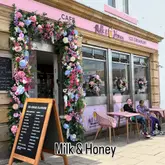 A bright, inviting shot of the Milk & Honey ice cream parlour in Seahouses, featuring a prominent floral archway entrance and outdoor seating.