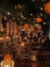 A wide-angle interior shot of a restaurant featuring warm, ambient lighting, hanging lanterns, and a lush, decorated ceiling, capturing the cozy and vibrant atmosphere of the venue.