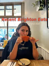 A lifestyle-focused cover image for a social media post featuring a woman drinking from a mug in a cafe setting, used to introduce a list of vegan dining recommendations in Brighton.