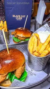 The video showcases the 'Soccer Saturday' experience at Black Cat Club in Liverpool, highlighting the bottomless drink offer, food options like burgers and pizzas, and competitive socialising activities such as shuffleboard and darts.