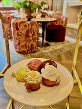 A high-quality, well-composed shot of a selection of delicate pastries served as part of an afternoon tea experience at a hotel venue. The image uses a shallow depth of field to isolate the food from the elegant, blurred interior background.