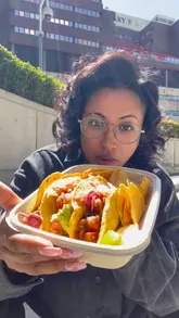 A creator reviews a Mexican street food truck called Hola Guacamole located in Paddington Basin. The video features the creator trying various tacos and a burrito, highlighting the freshness and flavour of the food while enjoying the sunny, waterside setting.