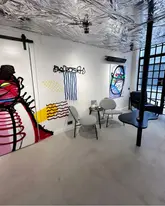 A clean, wide-angle interior shot of a restaurant space featuring modern, artistic decor, including graffiti-style wall art and a reflective metallic ceiling. The image captures the seating arrangement and the overall atmosphere of the venue.