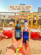 A bright, inviting 'cheers' shot featuring a variety of drinks, including cocktails and beer, held up against an outdoor venue background. The image effectively captures a social, fun atmosphere suitable for a bank holiday outing.
