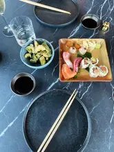 An overhead shot of a sushi brunch spread at Lucky Cat, featuring a platter of sushi and a side of cucumbers on a dark marble table.