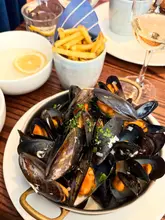 A close-up shot of a pot of moules frites served with a glass of rosé wine, capturing a casual dining experience at a restaurant.