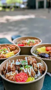 A short, energetic montage showcasing Japanese rice bowls being prepared and served at a market stall. The video focuses on the assembly of the dishes, highlighting fresh ingredients and toppings, before showing the exterior of the venue.