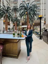 A professional brand ambassador portrait taken in the atrium of The Landmark London, featuring a woman standing beside a table displaying a selection of Perrier-Jouët champagne bottles. The image effectively communicates a luxury hospitality partnership.
