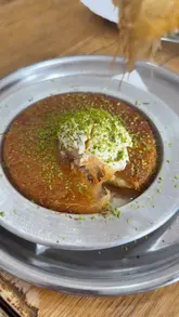 A montage video showcasing the preparation of Turkish tantuni and kunefe at Neco Tantuni in Enfield. The video features close-up shots of the cooking process, including the meat being cooked on a large flat pan, the assembly of the wraps, and the final plating with yogurt and butter. It also shows the preparation of a kunefe dessert with syrup and kaymak.
