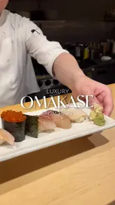A short, polished montage showcasing an omakase dining experience at INÉ. The video features close-up shots of various sushi and sashimi courses being prepared and served at an intimate counter, accompanied by text overlays detailing the price point.