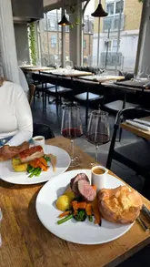 A high-quality food review video featuring a Sunday roast at a restaurant called Salut. The video highlights the food presentation, including roast meats, sides, and desserts, alongside the restaurant's open kitchen and interior.