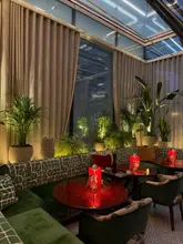 A high-quality, atmospheric interior shot of a restaurant, showcasing the elegant seating area, warm lighting, and lush greenery. The image effectively captures the upscale, intimate vibe of the venue.