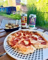 A high-quality, appetizing shot of a pepperoni pizza and garlic doughballs paired with craft beer, set against a scenic canal-side backdrop.