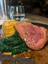 A high-quality, close-up food photograph featuring a perfectly cooked fillet steak, potato pavé, and black cabbage. The image uses a shallow depth of field to isolate the dish, highlighting the texture and quality of the ingredients, making it look highly professional and appetising.