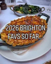 A high-quality, appetizing close-up shot of a golden-brown, flaky-crust pie served in a cast-iron skillet, accompanied by a side of greens in the background. The image is well-composed and clearly highlights the texture and quality of the food.