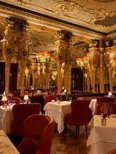 A stunning, wide-angle shot of the iconic, gilded dining room at Hotel Café Royal, showcasing its opulent, historic interior design and elegant table settings.