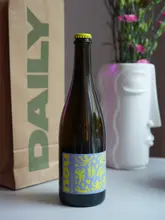 A clean, professional product shot featuring a bottle of 'nou secco brut' wine. The bottle is centered in the frame, flanked by a branded 'DAILY' paper bag and a decorative white vase with flowers, creating a lifestyle-focused aesthetic that feels intentional and well-styled.