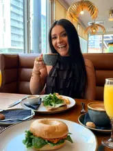 A bright, lifestyle-focused shot of a woman enjoying brunch at a hotel venue. The image captures a relaxed morning atmosphere with coffee and brunch dishes, though the framing of the food is slightly compromised.