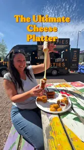 A short, punchy video featuring a creator presenting an 'Ultimate Cheese Platter' from a street food vendor. The video highlights various fried cheese items, including a giant mozzarella stick with a cheese pull, mac and cheese bites, brie bites, halloumi fries, and chilli cheese nuggets, set against the backdrop of the food truck.