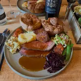A high-angle, appetizing shot of a classic Sunday roast dinner served in a pub setting, featuring sliced beef, large Yorkshire puddings, roast potatoes, and various vegetables.