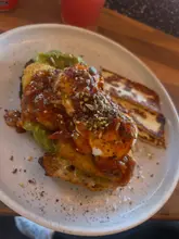 A top-down, close-up shot of a brunch dish featuring poached eggs, avocado, hash browns, and halloumi on toast, served on a speckled plate.