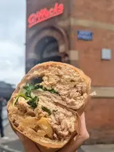 A close-up, eye-level shot of a sandwich held in front of the Afflecks building in Manchester, showcasing the cross-section of the filling.