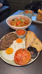 A montage of various dishes including steak and eggs, crispy chicken noodles, Kinder pancakes, and Biscoff French toast, accompanied by cocktails.