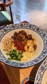 A short-form video review of JWD Hand-Pulled Noodle Bar in Cambridge, featuring shots of the ordering kiosk, the open kitchen, and various noodle dishes and a Chinese burger (rougamo).