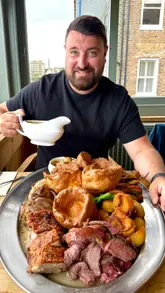 A short, visually appealing clip featuring a man pouring gravy over a large sharing platter of Sunday roast meats, including beef, chicken, lamb shank, and pork belly, accompanied by Yorkshire puddings and roast potatoes.