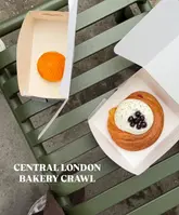 A clean, overhead shot of two pastries in takeaway boxes resting on a green metal bench, captured during a Central London bakery crawl. The lighting is bright and natural, highlighting the textures of the pastries.