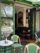 A shot of the entrance and outdoor seating area of Parosna restaurant, featuring green bistro chairs and a view into the warm, inviting interior.