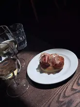 A close-up shot of a small plate of fried food, likely Olive all'Ascolana, served with a side of white wine in a dimly lit restaurant setting.