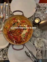 A high-quality, top-down photograph of a lobster pasta dish served in a cooking pan, placed on a marble-topped table with cutlery, glassware, and a lit candle, creating an inviting dining atmosphere.