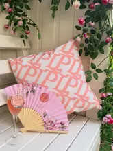 A promotional still image featuring a glass of Laurent-Perrier champagne placed on a white wooden bench, accompanied by a branded floral fan and a patterned cushion. The setting is styled to look like a summer garden pop-up, using soft, natural lighting to create an inviting, upscale atmosphere.