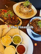 A flat-lay photograph of a pub meal spread featuring a chicken stack, halloumi fajitas, and loaded fries at The Tinsmith.