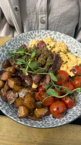 A short, handheld video showcasing a brunch spread at a cafe, featuring close-up shots of a steak bowl, poached eggs on toast, and a banana pudding dessert.