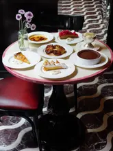 A high-quality, overhead shot of a table spread featuring a variety of desserts, including tarts, a chocolate dessert, and creme brulee. The presentation is elegant and inviting, set against a stylish interior with a distinctive patterned floor.