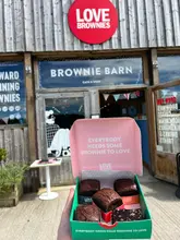 A first-person perspective shot holding a box of brownies in front of the Love Brownies shop, showcasing the product in its branded packaging.