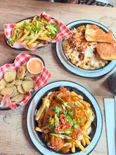 A top-down shot of a pub meal featuring mac and cheese, loaded fries, and fried pickles. The image captures a casual dining experience with generous portions, though the framing is tight.
