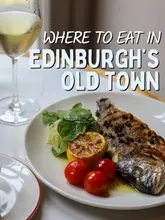 A high-quality, well-composed food photography shot featuring a grilled fish dish with cherry tomatoes and a glass of white wine, used to promote a restaurant in Edinburgh's Old Town.
