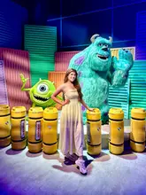 A bright, high-energy photo of a creator posing in front of a Monsters, Inc. themed display at an interactive exhibition. The image captures the vibrant, colourful set design, effectively showcasing the venue's immersive nature and appeal for fans of the franchise.