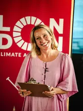 A portrait of a woman smiling and holding a clipboard, captured at an event for London Climate Action Week at 12th Knot.