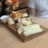 A casual, amateur-style photograph of a cheese and bread sharing board served on a wooden platter. The image captures a simple, rustic food offering, likely taken in a cafe or restaurant setting.