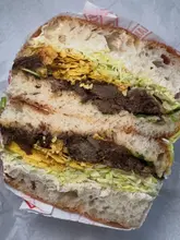 A top-down, close-up shot of a sandwich cut in half, revealing layers of meat, shredded lettuce, and crushed crisps inside a rustic bread roll.
