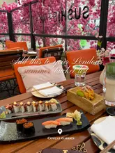 A high-quality, well-composed flat lay shot of a sushi spread at a restaurant terrace, featuring vibrant cherry blossom decor. The image effectively captures the upscale, aesthetic atmosphere of the venue, making it highly appealing for a summer dining occasion.