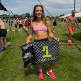 A photo of a woman holding a first-place flag at the Turf Games fitness competition, standing on a grass field.
