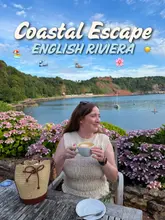 A high-quality lifestyle shot featuring a woman enjoying a coffee at an outdoor table with a scenic coastal view, effectively promoting a stay at a seaside inn.